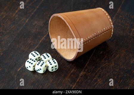 Leather dice cup and dice on the table, rolling all sixes with 5 dice representing gambling and luck Stock Photo
