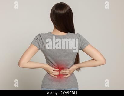 Woman suffering from pain in lower back on light background Stock Photo