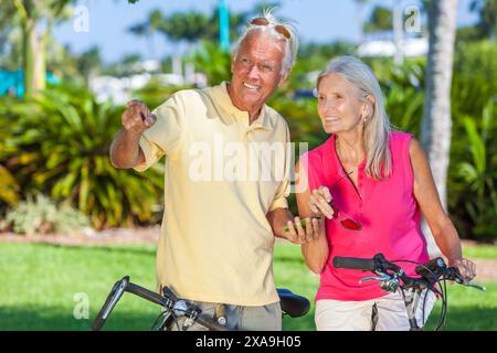 Happy senior man and woman couple together cycling on bicycles in a park old man and woman using an app on a cell phone Stock Photo