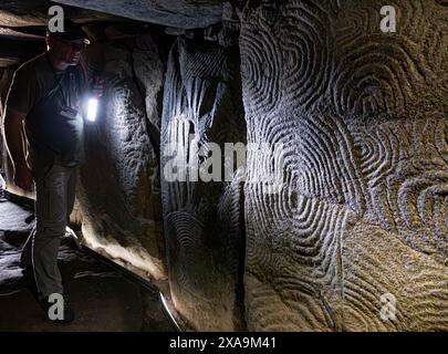 GAVRINIS CAVE  TOUR GUIDE TORCHLIGHT STONE CARVINGS TEXTURE INTERIOR Brittany France, prehistoric cairn, dolmen, dry stone grave, with renowned symbolic and mysterious Stone Age carvings. One of the most outstanding examples of earliest architecture in the Western World. Cairn de Gavrinis Sagemor Cale de Penn-Lannic, Larmor Baden Brittany France (Megalithes du Morbihan) Stock Photo