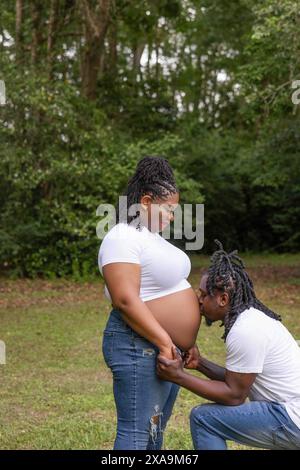 A beautiful African-American couple posing for maternity portraits with the dad kneeling and kissing mom's stomach. Stock Photo
