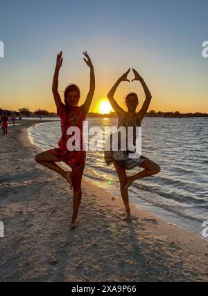 Two women practicing yoga on Crete island beach during sunset Stock Photo