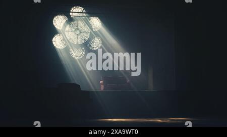 Sunlight streams through a flower shaped window into a dark room with a -table Stock Photo