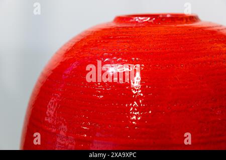 An empty round red vase stands in front of white wall, close up photo with selective soft focus Stock Photo