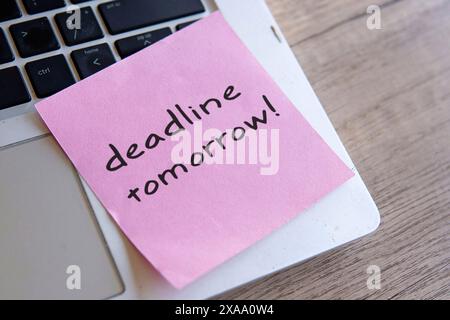 Sticky note with the word "deadline tomorrow" on a laptop keyboard. Stock Photo
