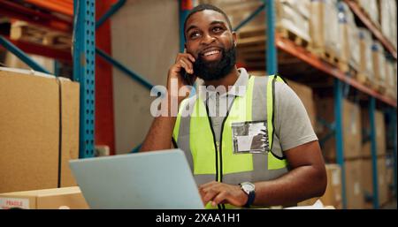 Man, phone call and talking for distribution in factory and order on laptop for shipping solutions. African worker, smile and cellphone for networking Stock Photo