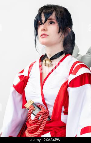 A female cosplayer in a white and red outfit with black hair and a bell around her neck, posing Stock Photo