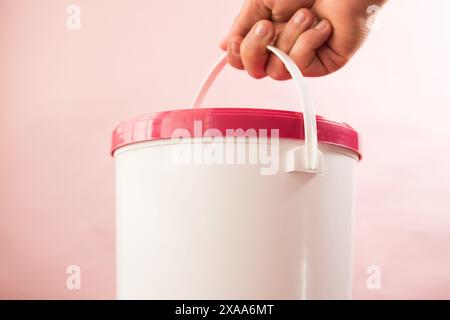 A hand holding a white plastic bucket with a red lid Stock Photo