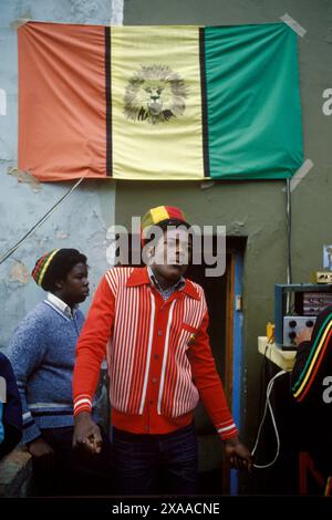 Young black 1970s British Rastafarian dancing to a sound system under a version of the Lion of Judah flag, that represents Haile Selassie I, Emperor of Ethiopia. He is wearing a Gabicci style jumper. There is no 'G' motif on the pocket, so this may be a copy. Notting Hill, Carnival, London, England 27th August 1979. UK HOMER SYKES Stock Photo