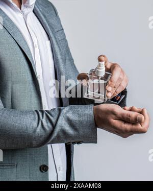 Man holding up bottle of perfume. Men perfume in the hand on suit background. Handsome man in formal suit and with bottle of perfume, closeup. Fashion Stock Photo