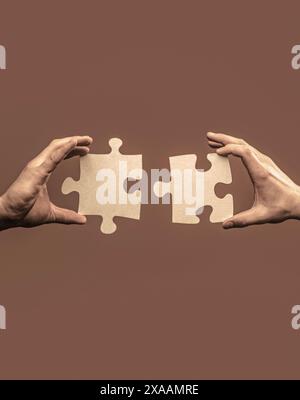 Closeup hand of connecting jigsaw puzzle. Men holding and putting a piece of jigsaw puzzle together. Two hands trying to connect couple puzzle piece Stock Photo