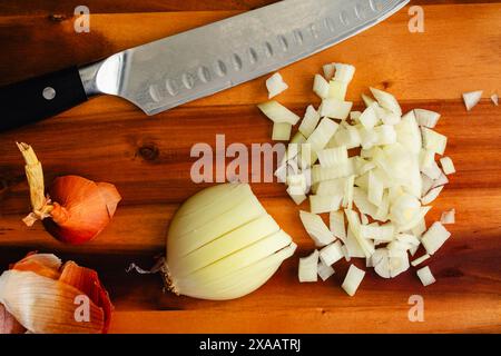 Dicing a Peeled Yellow Onion: Diced onion on a wooden cutting board with a chef's knife and peels on the side Stock Photo