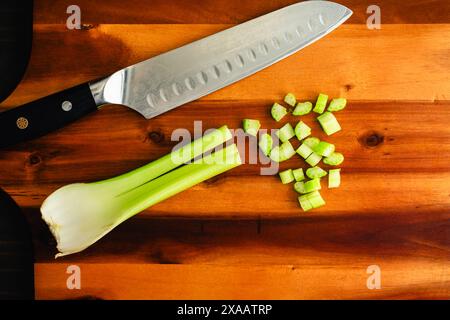 Dicing a Stalk of Celery: Diced celery on a wooden cutting board with a chef's knife on the side Stock Photo