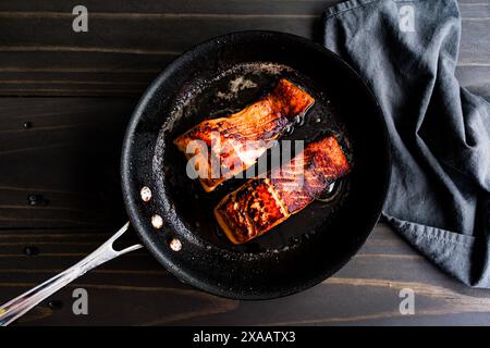 Seared Salmon Fillets in a Small Non-stick Skillet: Two salmon fish fillets browned olive oil and butter in a skillet placed on a dark wooden table Stock Photo