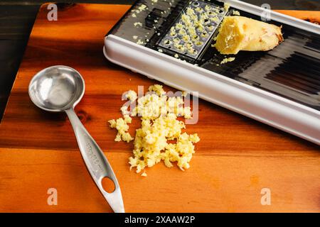 Grated Ginger with a Grater: A tablespoon of grated ginger on a wooden cutting board with a mandoline Stock Photo