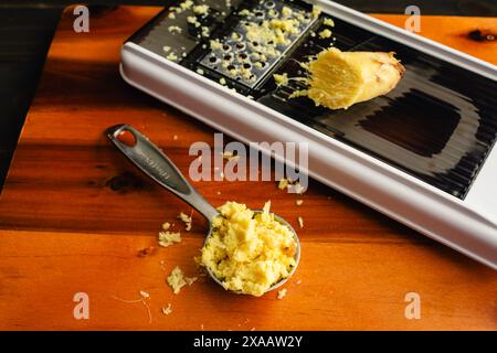 Tablespoon of Grated Ginger with a Grater: A measuring spoon of grated ginger on a wooden cutting board with a mandoline Stock Photo