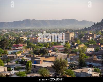 Scenic panoramic view of a small town nestled near mountains in Pakistan, showcasing residential buildings, lush greenery, and a tranquil environment Stock Photo