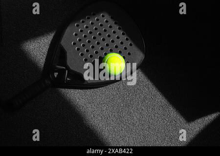 Black professional paddle tennis racket and ball with natural lighting on black background. Horizontal sport theme poster, greeting cards, headers, we Stock Photo