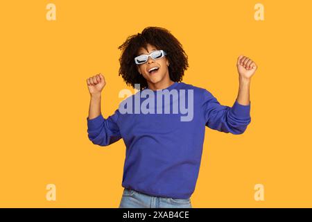 Happy Young Guy Wearing Sunglasses Dancing Against Yellow Background Stock Photo