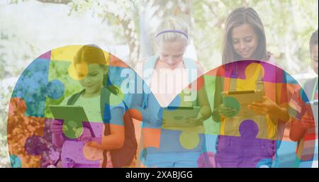 Image of colourful puzzle pieces and heart over kids friends using electronic devices Stock Photo