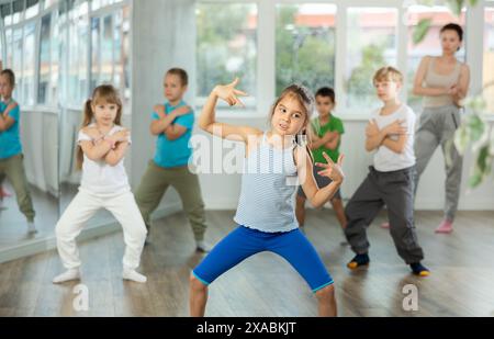 Positive juvenile girl engaged in breakdancing in training room with children's group Stock Photo