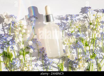 Cosmetic glass transparent bottle with dropper for hyaluronic acid among different spring wildflowers on a white background. Beautiful light reflectio Stock Photo