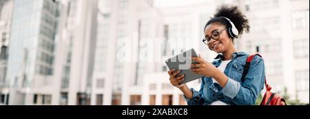 Happy Black Woman Student Using Tablet Computer Wearing Headphones Outside Stock Photo