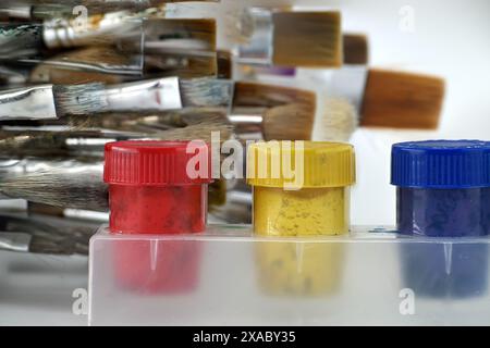 Array of paintbrushes of different sizes and colors alongside cans of acrylic paint with visible colors isolated on a white background Stock Photo