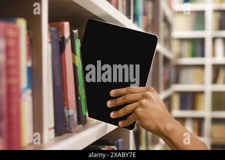 Afro student placing digital tablet on bookshelf Stock Photo
