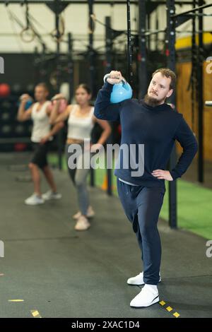 Bearded man doing kettlebell overhead shoulder press in gym Stock Photo