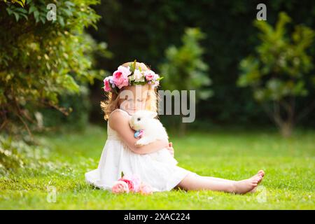 Little girl bunny in sunny garden. Summer blooming park. Child holding rabbit at Easter celebration. Egg hunt. Stock Photo