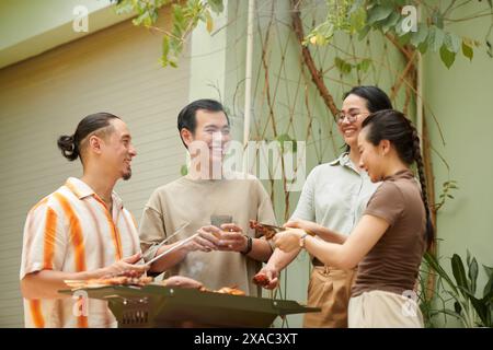 Joyful friends chatting and joking around when having barbeque in backyard Stock Photo