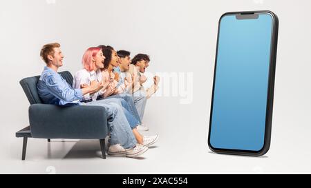 Multiracial group sitting on couch, looking at huge phone Stock Photo