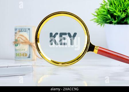 KEY text through a magnifying glass on a gray background in a composition with dollar bills, a calculator and a flower Stock Photo