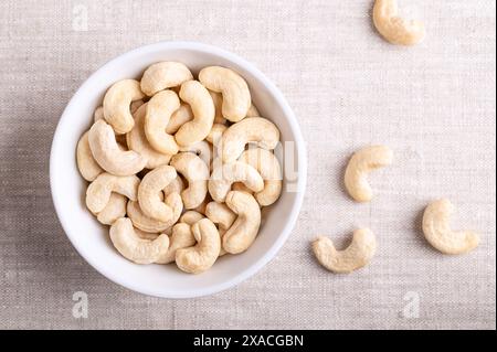 Cashew nuts, raw cashews in a white bowl on linen fabric. Seeds of shelled fruits of cashew tree Anacardium occidentale. Stock Photo