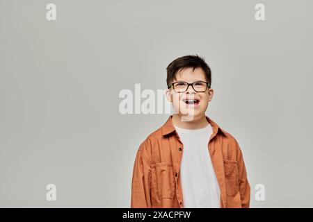 A little boy, with Down syndrome, wearing glasses, stands against a gray background. Stock Photo