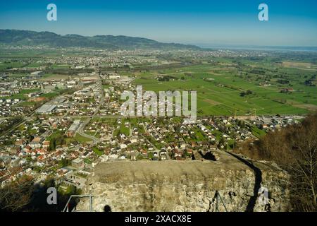 A city view with a large green field in the background. The city is full of houses and buildings, and the sky is clear and blue Stock Photo