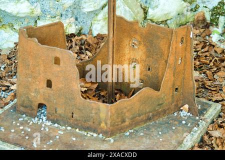 A small, rusted structure made of metal sits on a stone slab. The structure is in the shape of a building, with a roof and a chimney Stock Photo