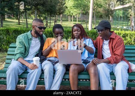 Happy black friends spending time together in nature, using portable computer watching funny videos Stock Photo