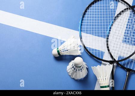 Feather badminton shuttlecocks and rackets on blue background, flat lay. Space for text Stock Photo