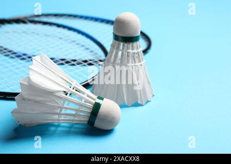 Feather badminton shuttlecocks and rackets on light blue background, closeup. Space for text Stock Photo