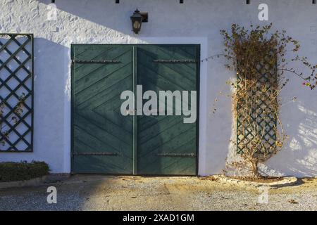 photography of an old traditional Alpine farmhouse with white walls and green wooden gates on sunny winter day Stock Photo