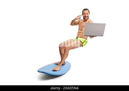 Full length shot of a surfer on a board smiling at camera and using a smartphone and a laptop computer isolated on white background Stock Photo