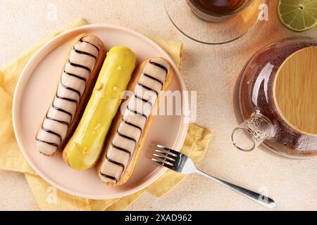 Different tasty glazed eclairs and tea served on color textured table, flat lay Stock Photo