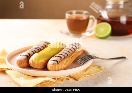 Different tasty glazed eclairs served on color textured table, closeup Stock Photo