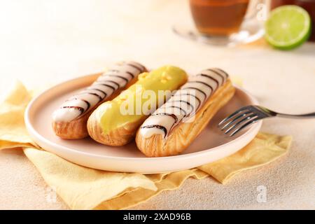 Different tasty glazed eclairs served on color textured table, closeup Stock Photo