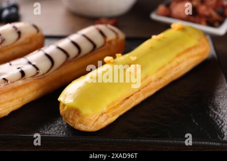 Plate with different tasty glazed eclairs on table, closeup Stock Photo
