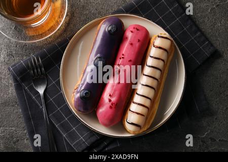 Different tasty glazed eclairs served with tea on grey textured table, flat lay Stock Photo