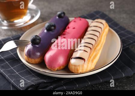 Different tasty glazed eclairs served on grey textured table, closeup Stock Photo