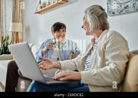 Two women engage in a deep conversation on a laptop while seated on a comfortable couch. Stock Photo